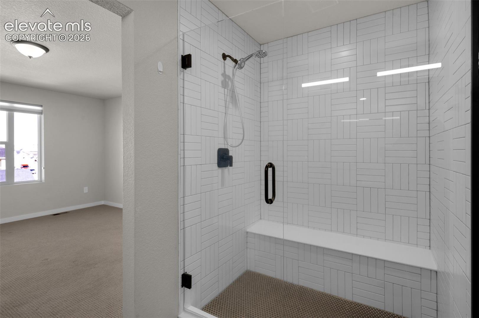 Shower enclosure with clear glass paneling, white subway tile surround, built-in bench, and dark bronze fixtures