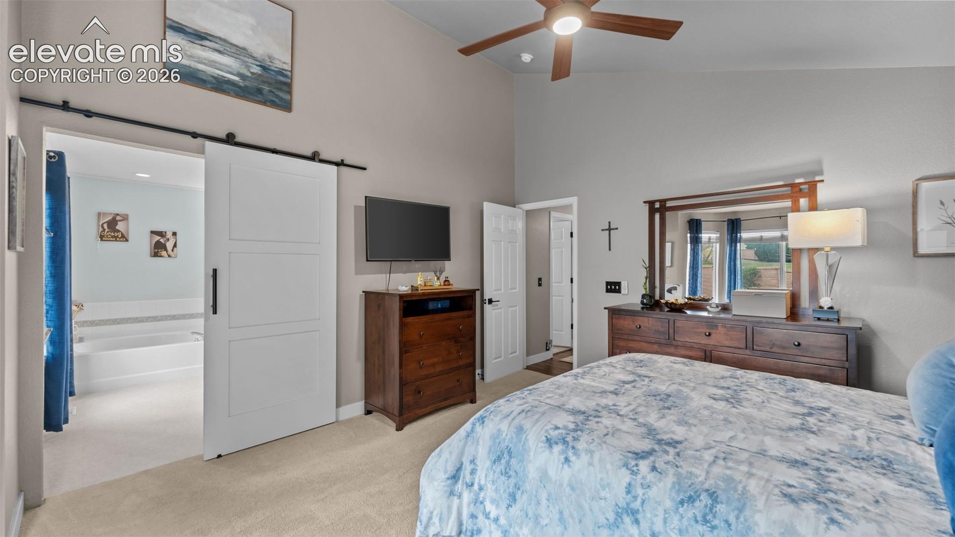 Vaulted ceilings with a ceiling fan, neutral wall paint, and a sliding barn-style door on a black metal track system