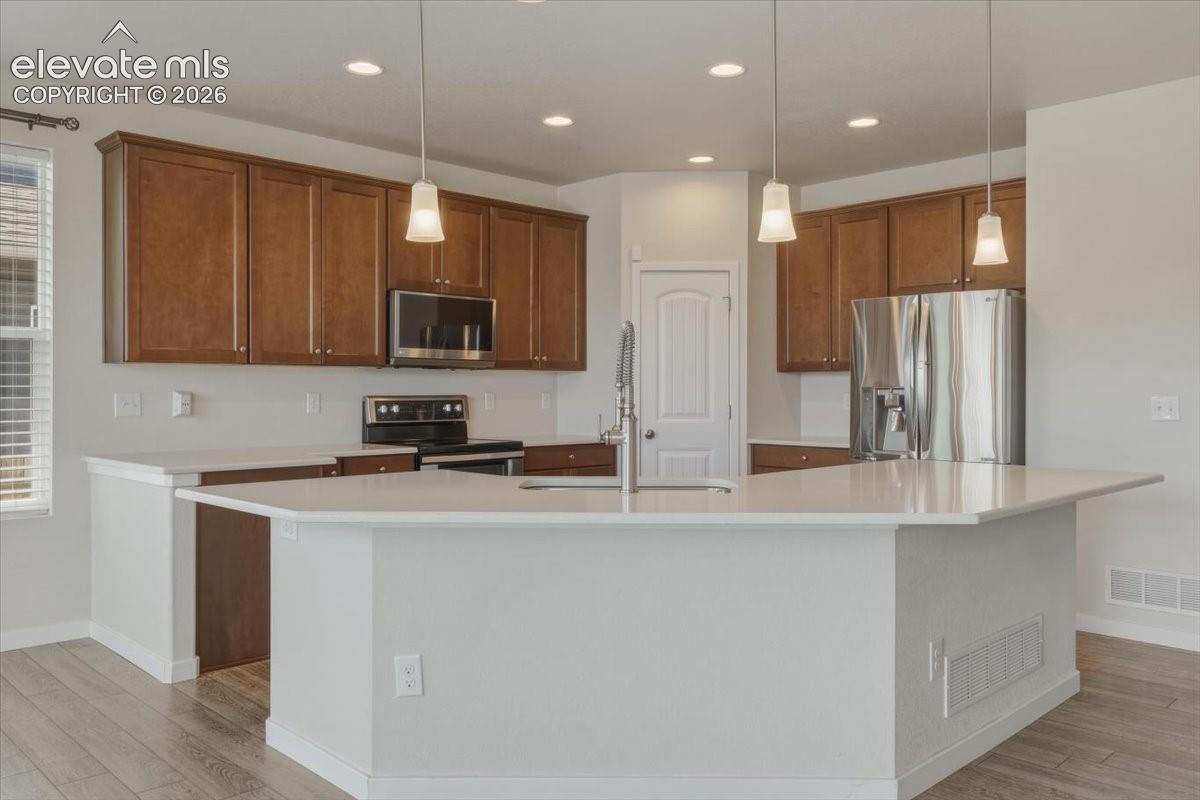 Kitchen featuring an expansive center island with pendant lighting, stone countertops, wood-finish flooring, stainless steel appliances, and abundant cabinetry