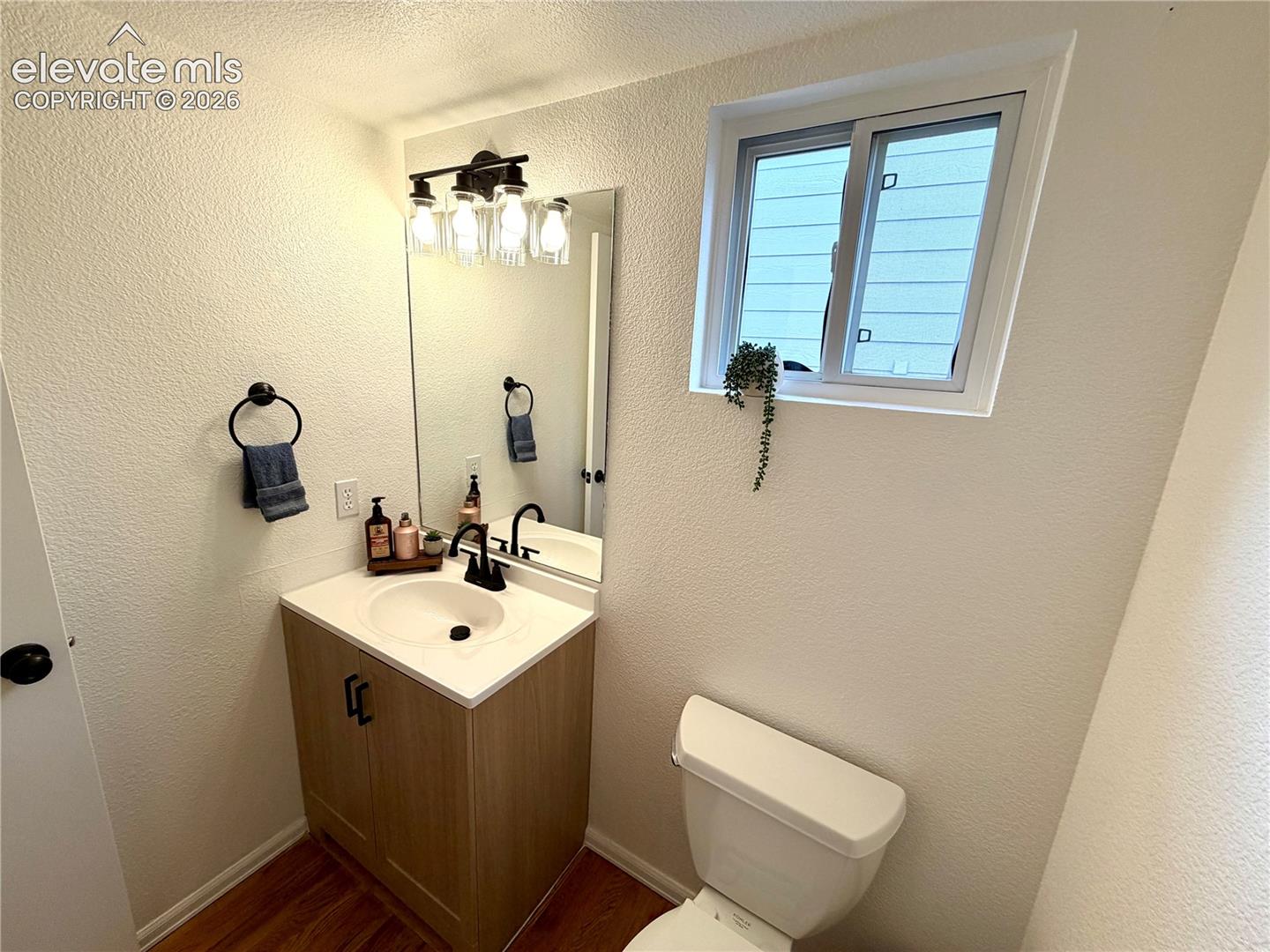 Bathroom featuring a light wood-finish vanity with a white countertop and integrated sink, black-finish faucet, and a rectangular mirror