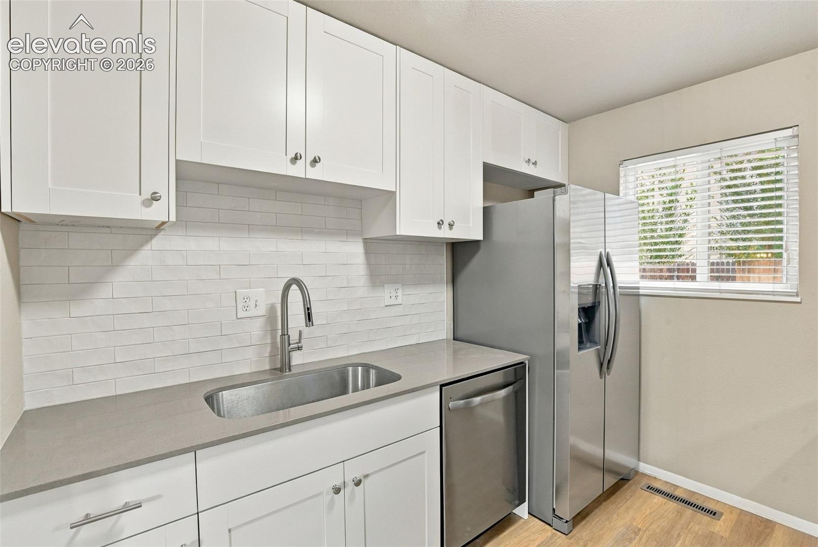 Kitchen featuring white shaker-style cabinetry, a light-toned quartz countertop, stainless steel undermount sink with a gooseneck faucet, white subway tile backsplash, and stainless steel appliances