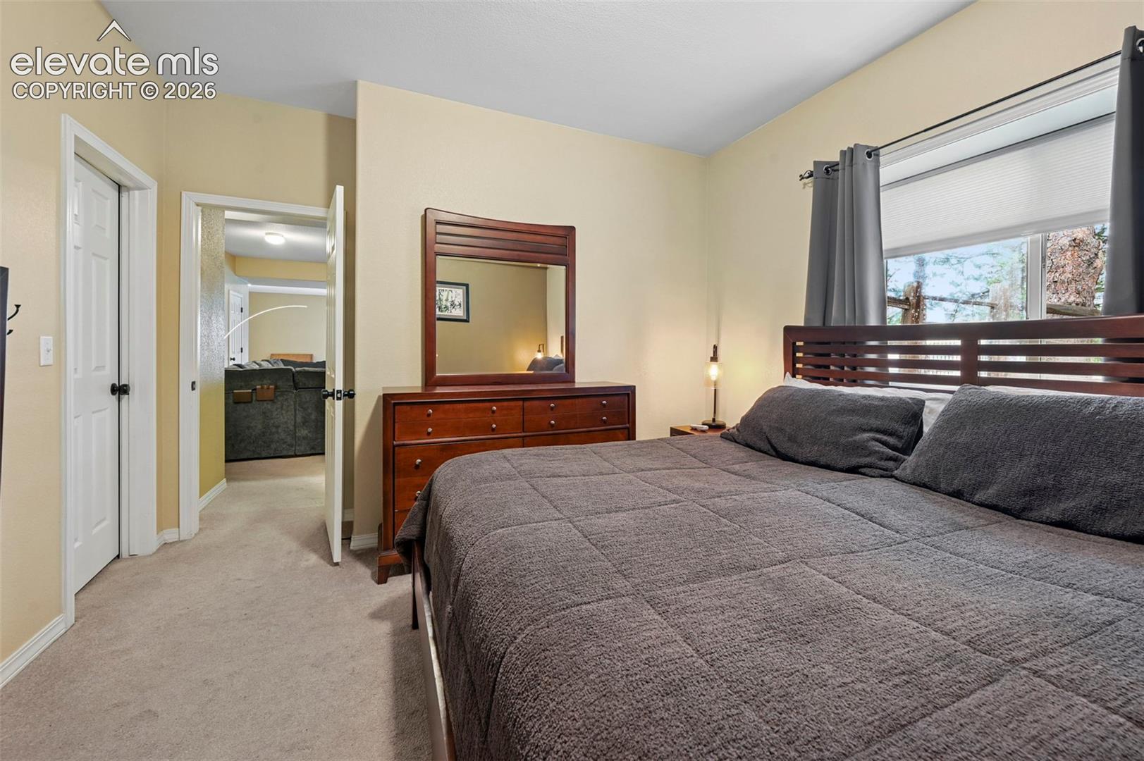 Carpeted flooring, a window with shades, a wooden headboard, and a wooden dresser with an attached mirror