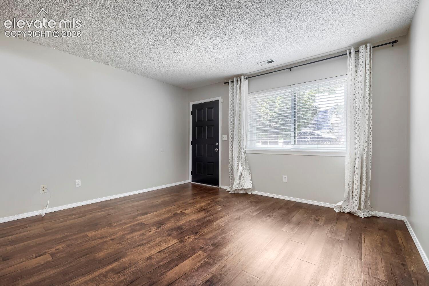 Living space featuring wood-finish flooring, a fireplace with decorative tile surround and white mantel, light gray wall paint, white baseboards, and a wooden staircase with white risers and railings