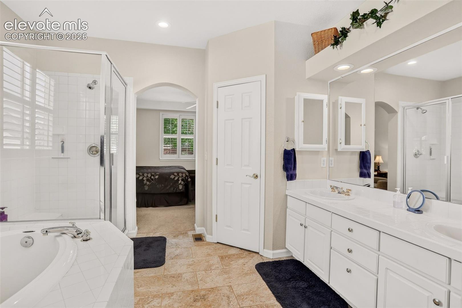 Dual vanity with integrated sinks, framed mirror, built-in medicine cabinets, tile flooring, and a glass-enclosed shower