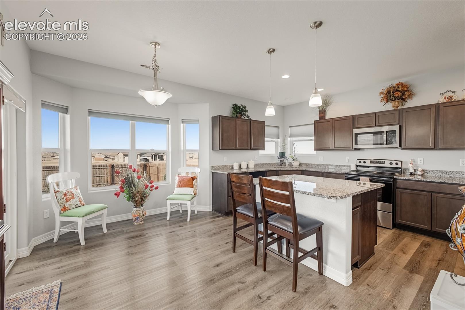 The gourmet kitchen featuring dark cabinetry, granite countertops, central island, LVP flooring, and pendant flooring. A corner sink offers extra natural lighting while the dining nook features a large bay windows with unforgettable mountain views. 