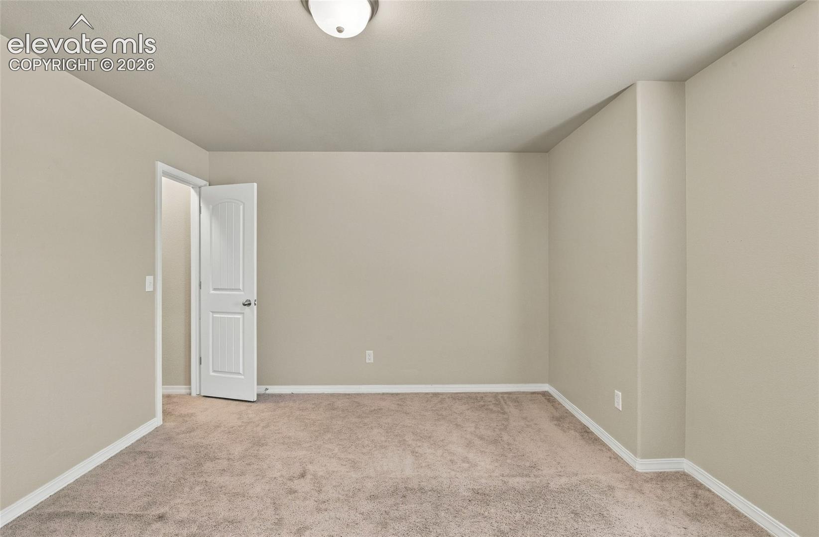 Neutral-toned interior room featuring wall-to-wall carpeting, a multi-panel interior door, and a ceiling-mounted light fixture