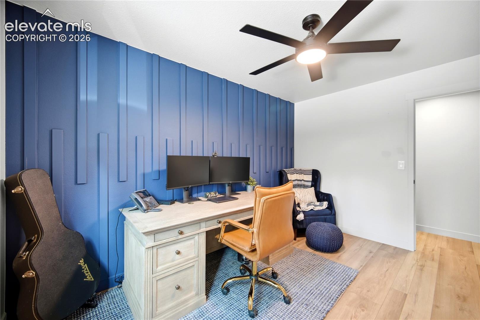 Room featuring blue vertical slat accent wall, light-toned wood-finish flooring, and a ceiling-mounted light fixture with integrated fan