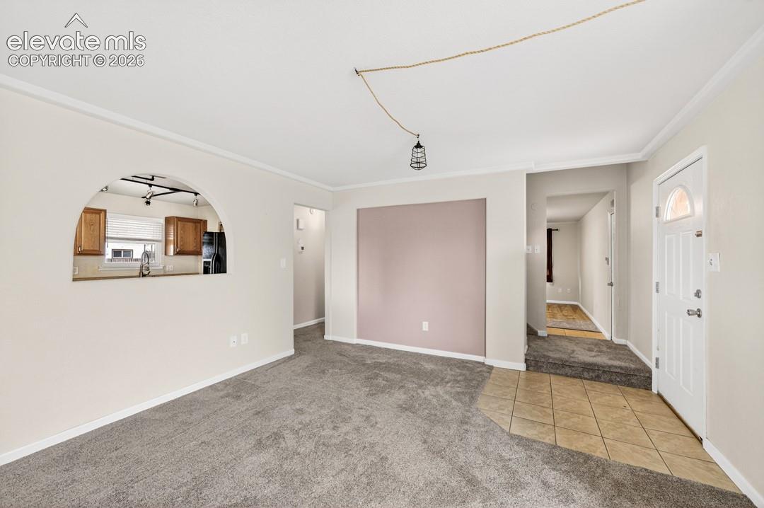 Carpeted living area with crown molding, arched passthrough to kitchen, and a front entry with tile flooring