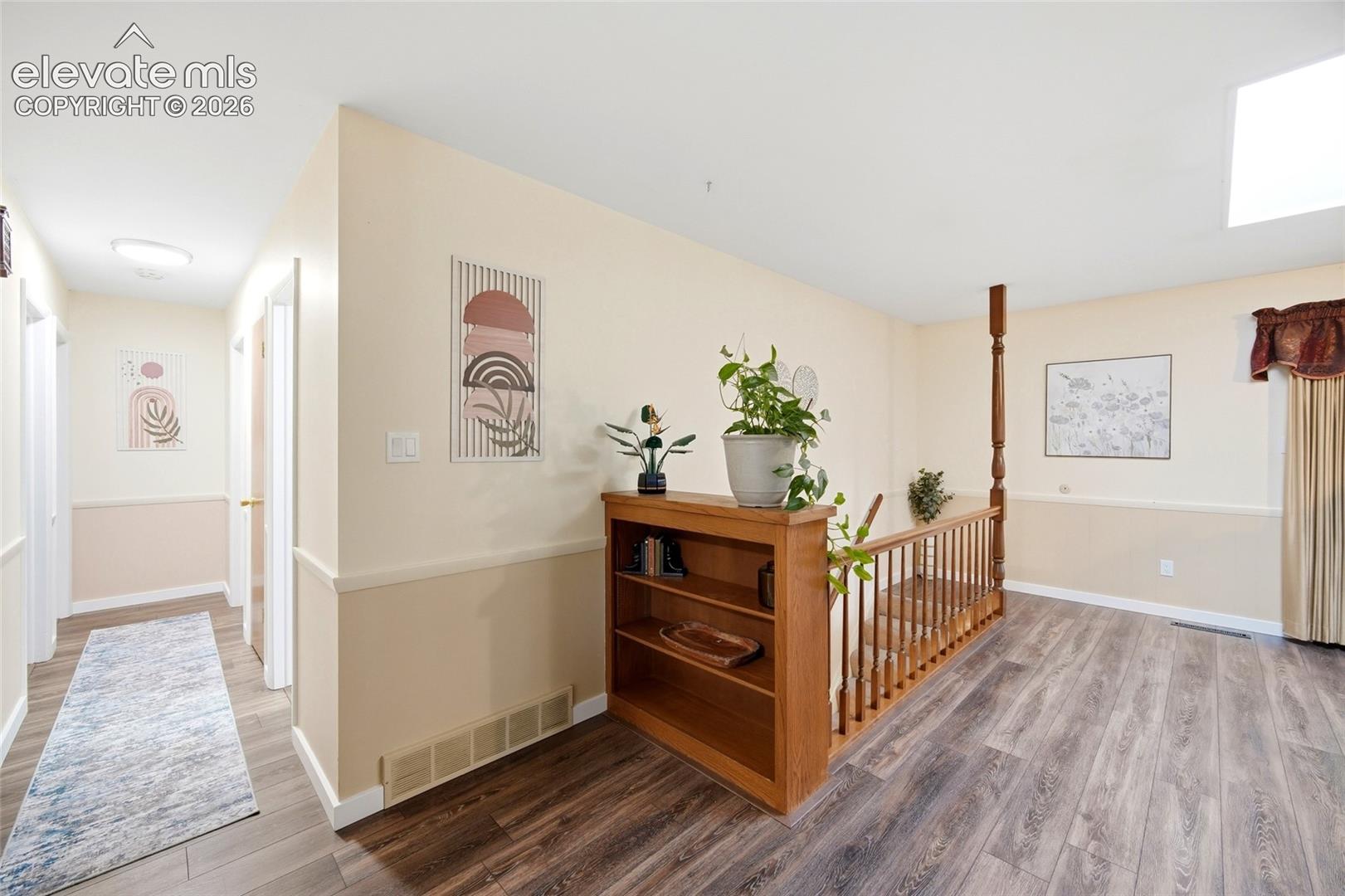 Interior space featuring wood-finish flooring, a built-in wooden bookcase, and a wooden stair railing with a decorative newel post