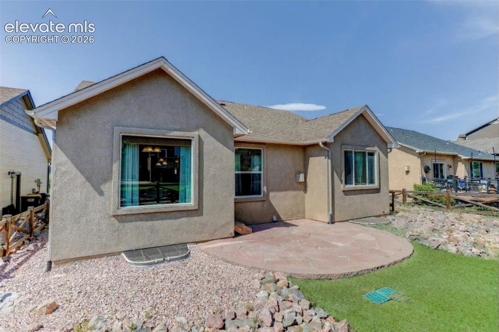 Stucco exterior with a pitched roof, featuring multiple windows, a stone patio, and artificial turf