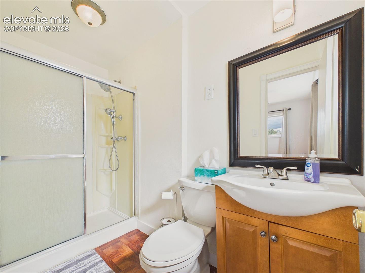Bathroom featuring a walk-in shower with sliding glass doors, an updated showerhead, a wood vanity, and a framed mirror.