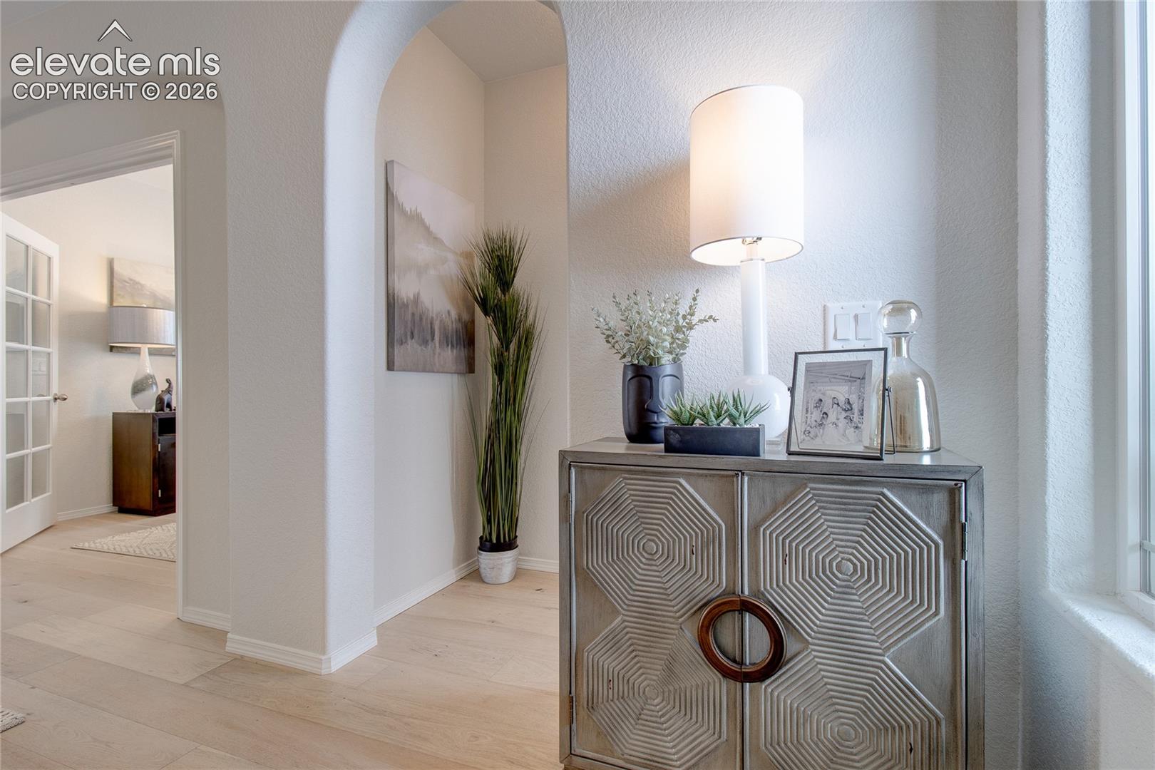 Arched architectural entryway featuring light-toned wood-finish flooring and textured wall surfaces