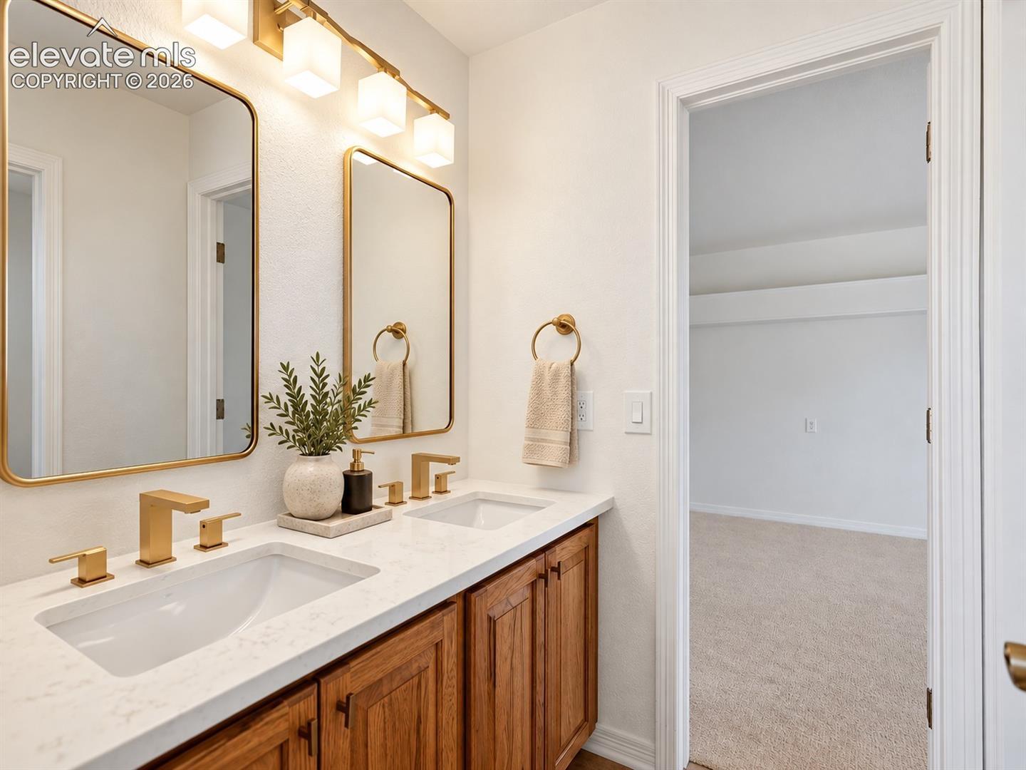 Dual-sink vanity featuring stone-patterned countertops, wood-finish cabinetry, metallic fixtures, and dual framed mirrors