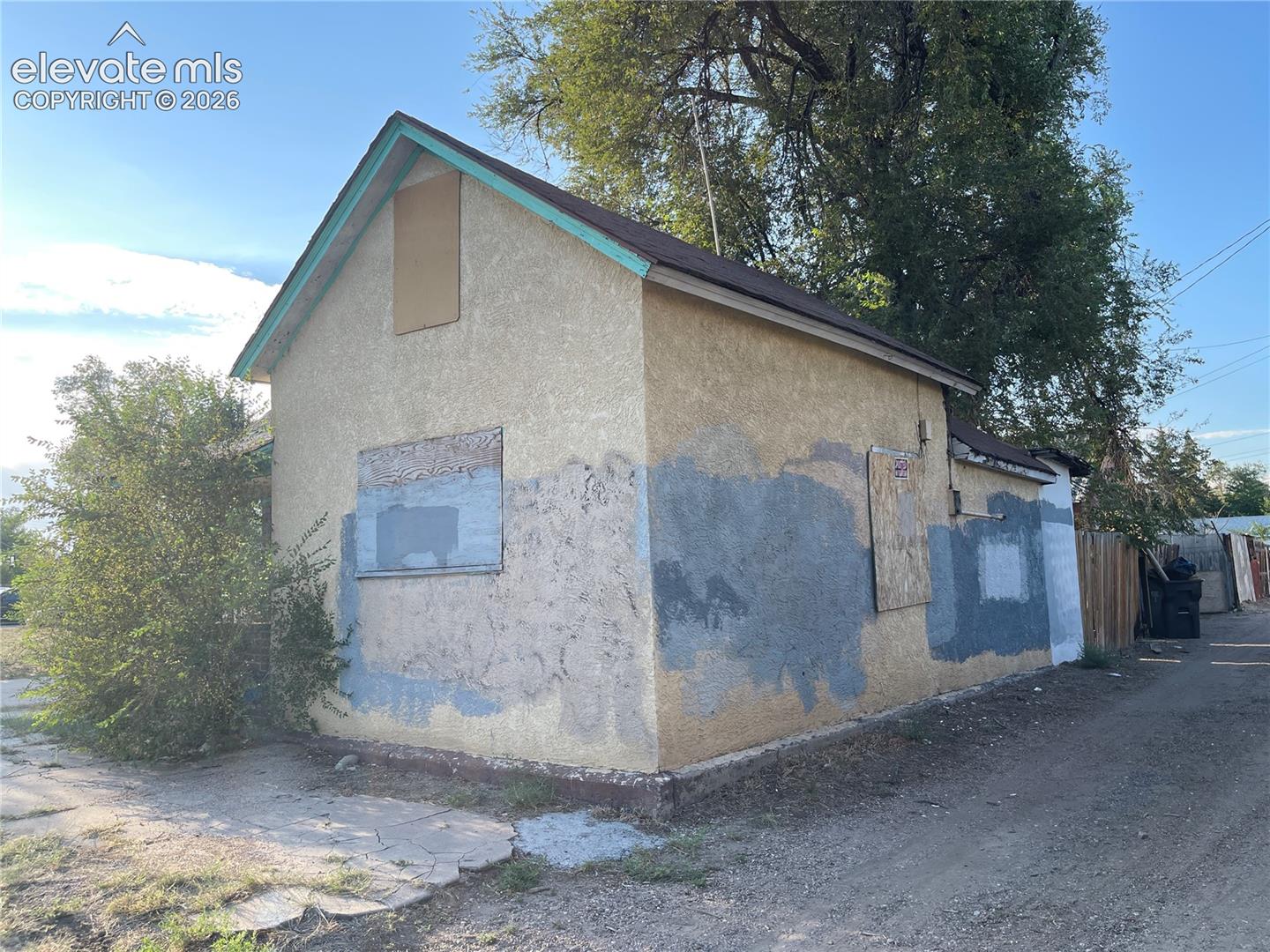 Detached structure with stucco exterior, gabled roofline, and wood-panel window covers
