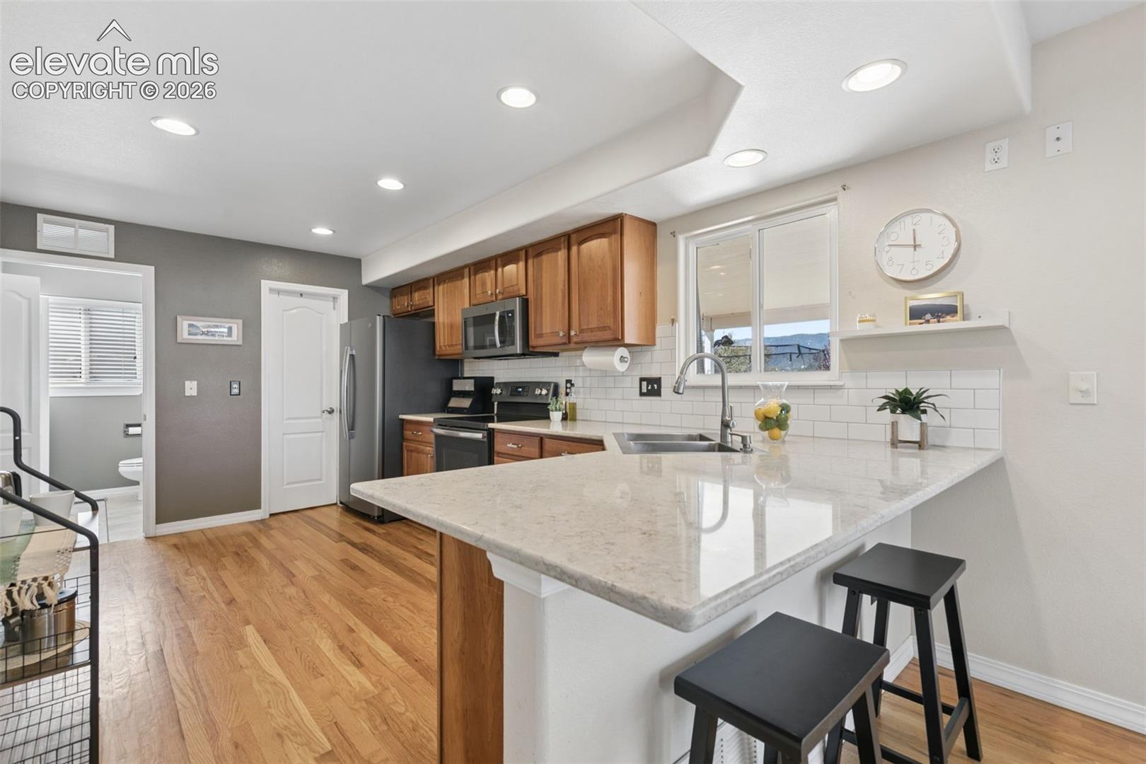 Kitchen with wood-finish flooring, recessed lighting, and a breakfast bar with stone countertops