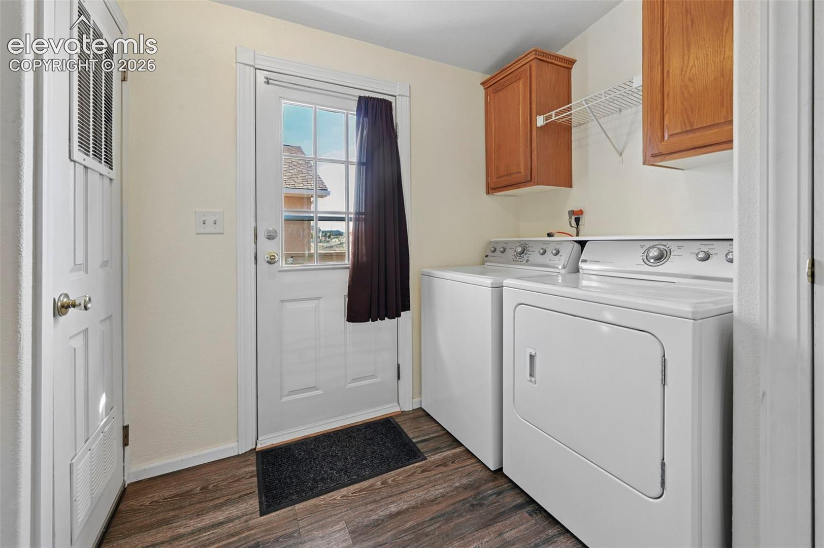 Laundry area featuring wood-finish flooring, upper wooden cabinetry, wire shelving, and a half-glass exterior door
