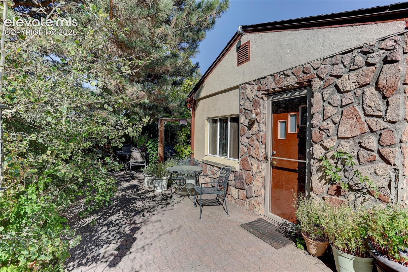 Patio area featuring interlocking paver stones, a stone-clad exterior, and a wood-finish entry door with multiple glass inserts