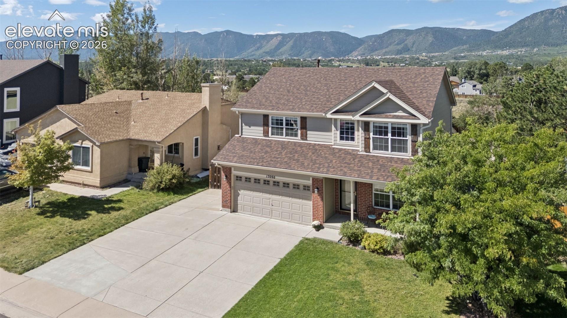 Two-story residence featuring a two-car garage, concrete driveway, front lawn, and mature trees
