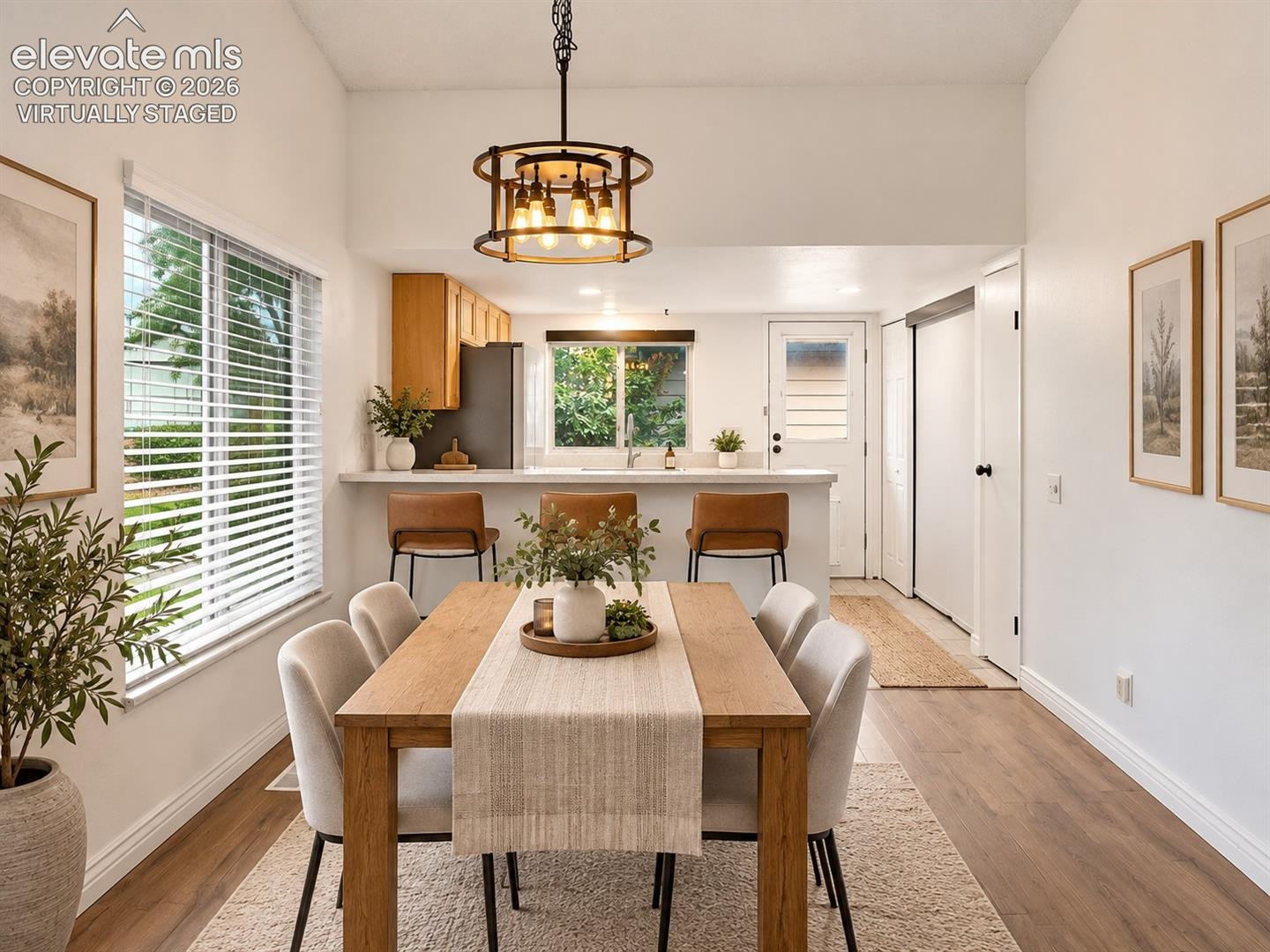 Dining area featuring wood-finish flooring, a drum-style chandelier with exposed bulbs, and a breakfast bar with stone-surfaced countertop- virtually staged