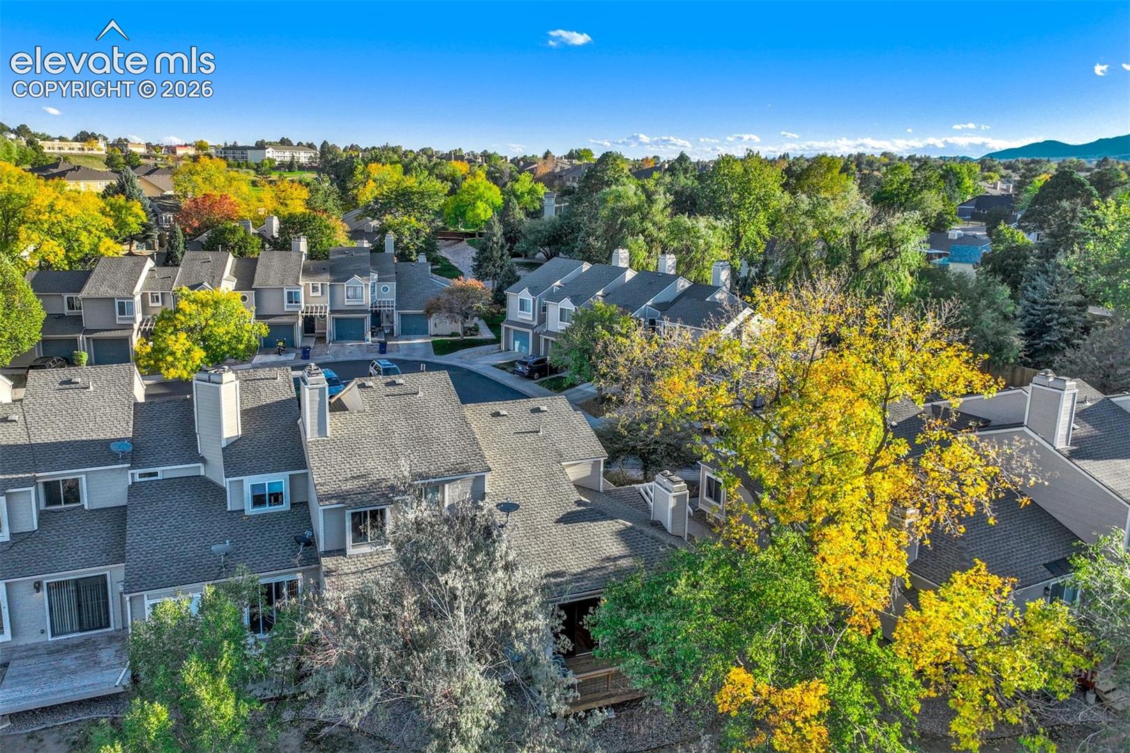 Aerial perspective featuring multi-story residences with shingled gable roofs, private wooden decks, and integrated garage doors, surrounded by mature deciduous trees and mountainous terrain