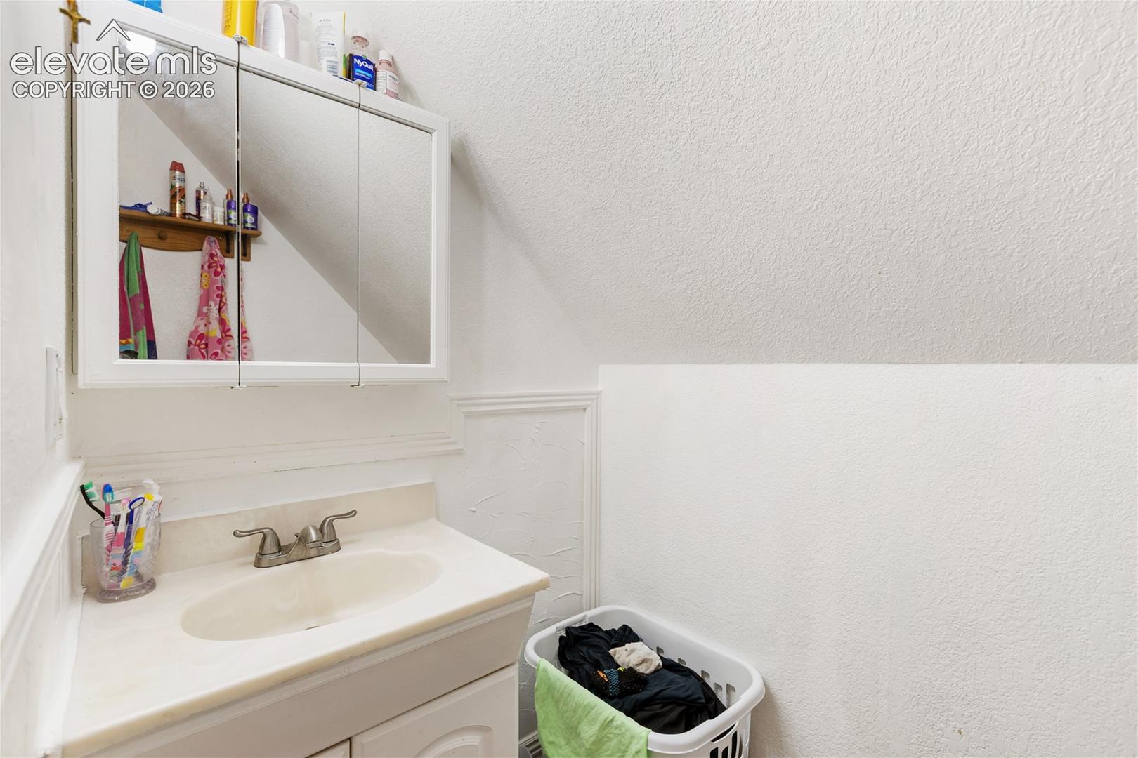 Vanity featuring a white cabinet base, integrated sink, and dual-handle metal faucet, complemented by a tri-fold medicine cabinet and decorative wall trim