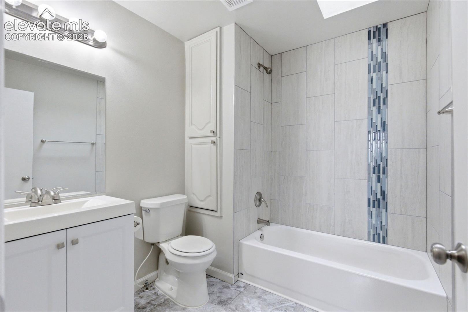 Bathroom featuring a shower-tub combination with a decorative tile accent, white vanity with integrated sink, chrome fixtures, and a tall built-in storage cabinet