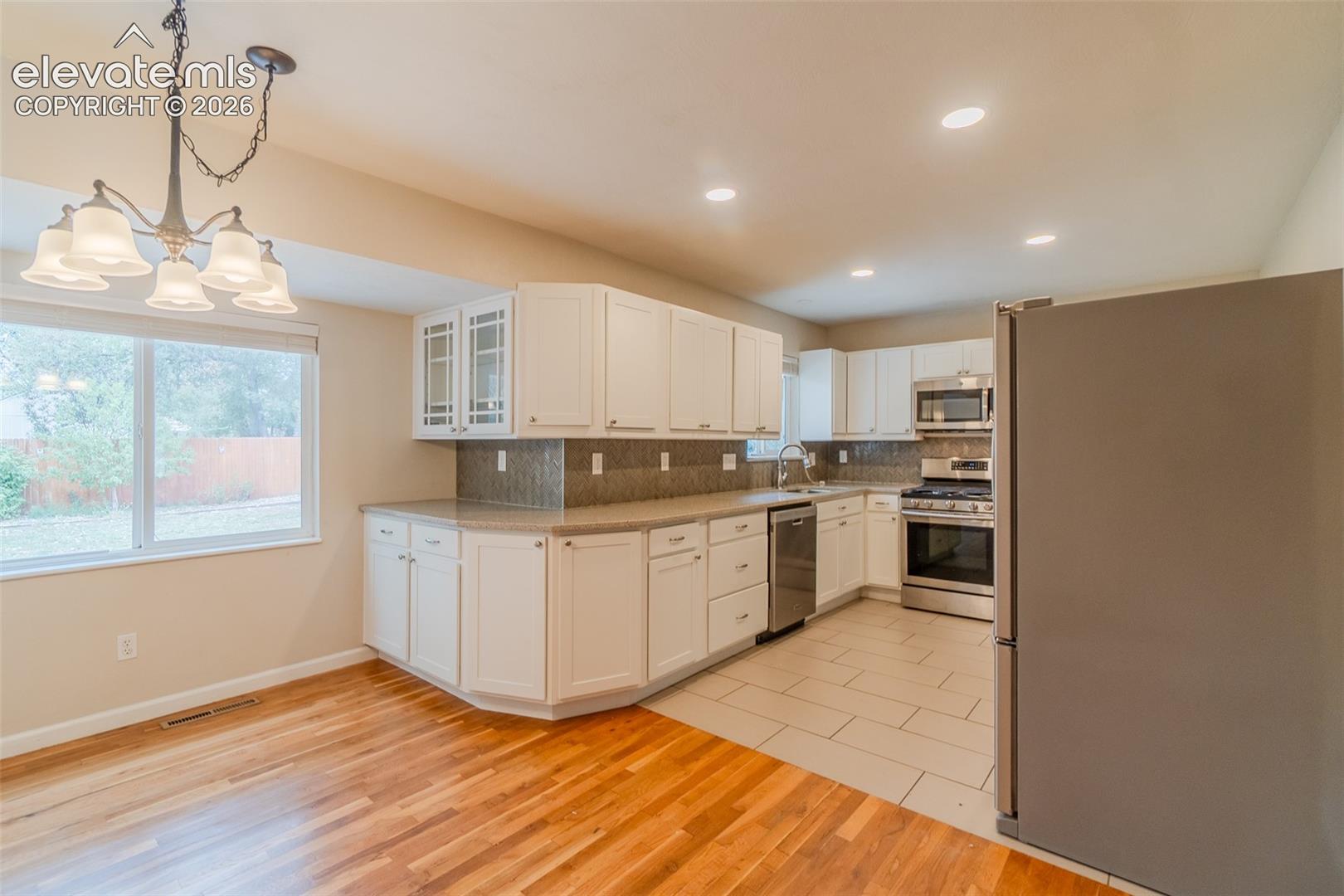 Kitchen featuring white cabinetry with some upper glass fronts, stainless steel appliances, and a tiled backsplash