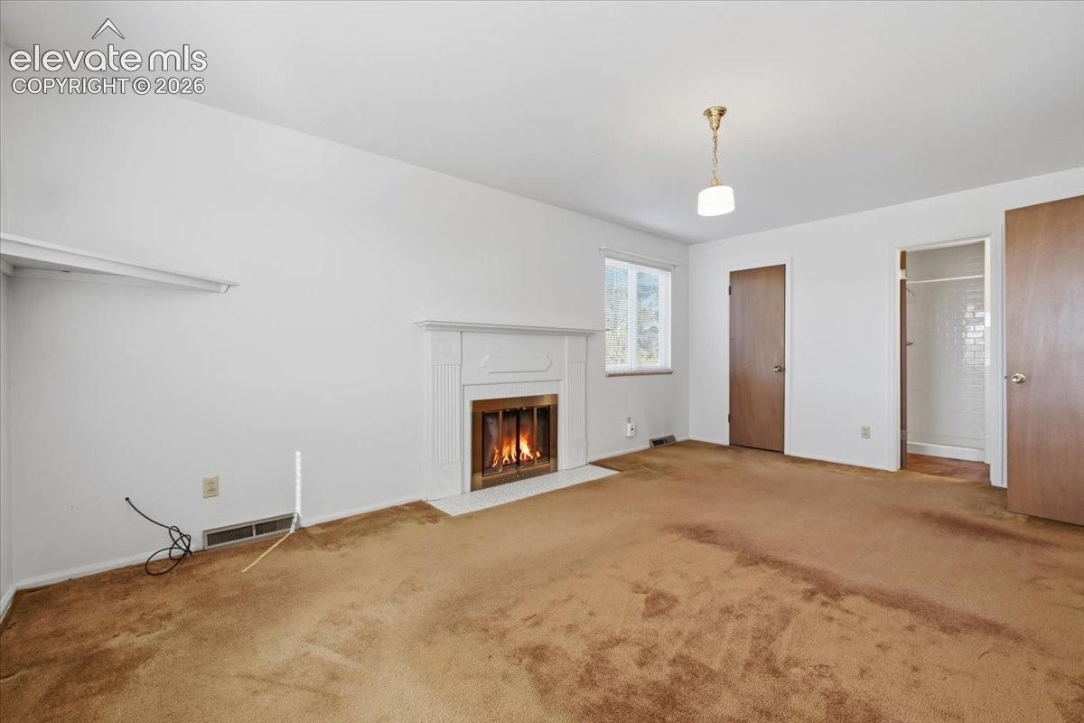 Fireplace with a classic mantel, wall-to-wall carpeting, and a single-light pendant fixture