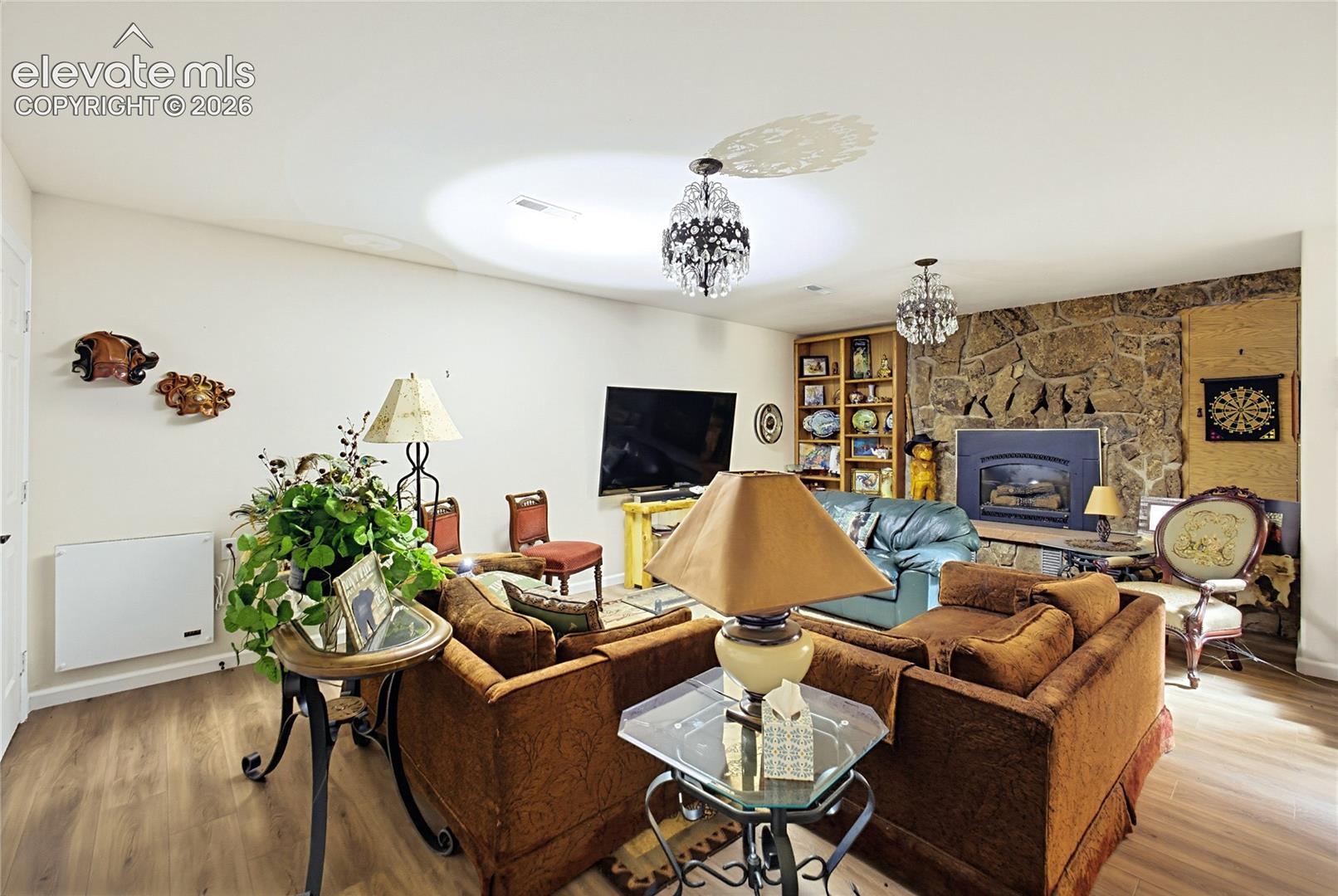 Living area featuring wood-finish flooring, a floor-to-ceiling stone fireplace, built-in shelving, and dual crystal chandeliers