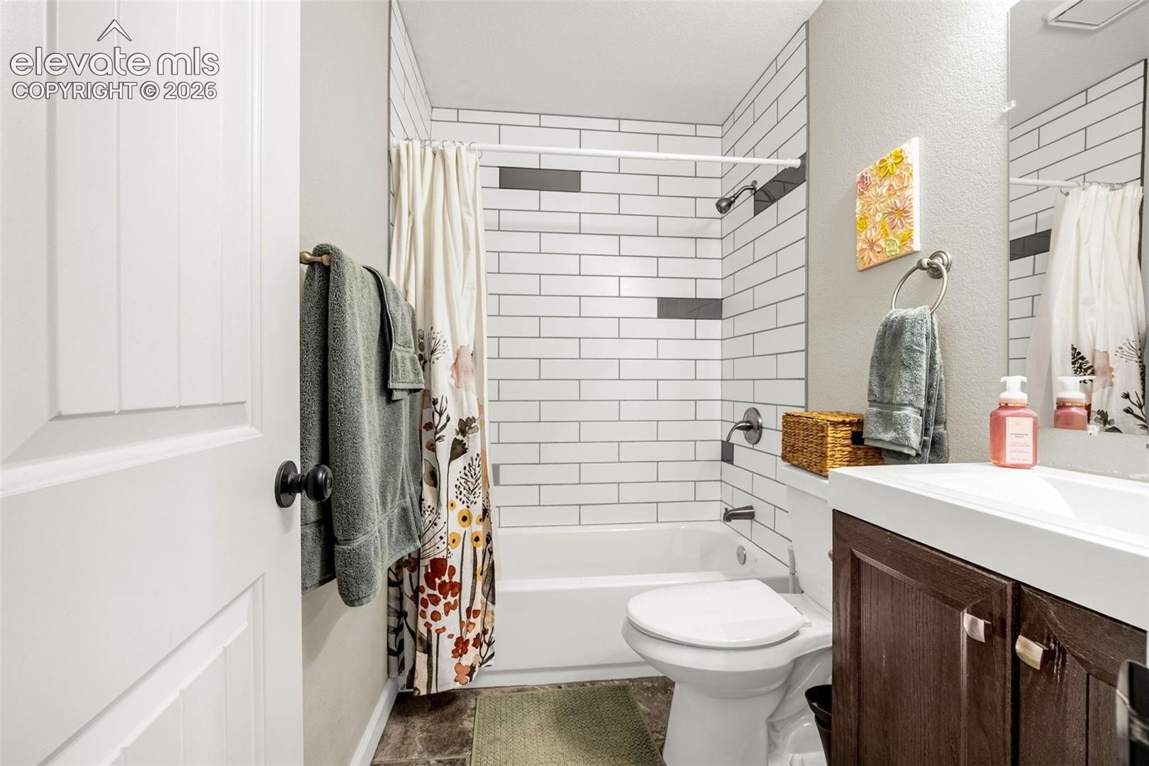Bathroom featuring white subway tile walls with horizontal charcoal accent detailing, a deep soaking tub, dark wood-finish vanity cabinetry, and a rectangular integrated sink
