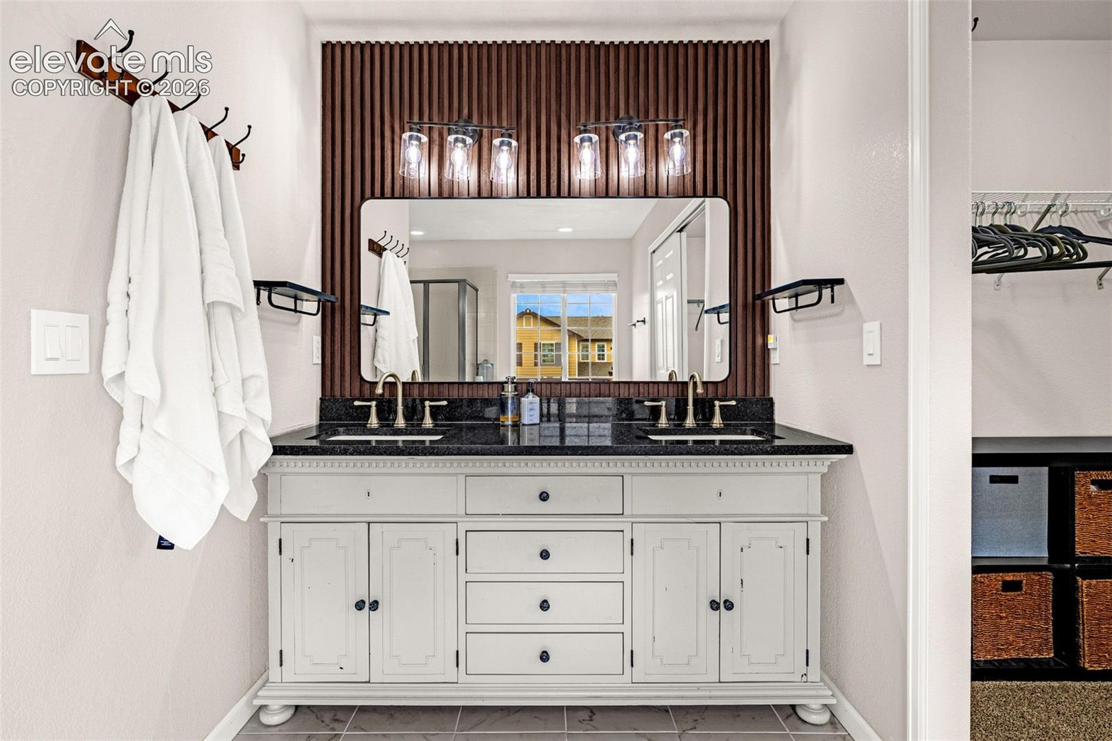 Double vanity featuring a stone countertop, under-mount sinks with metallic faucets, a vertical-slat accent wall, and a multi-bulb vanity light fixture
