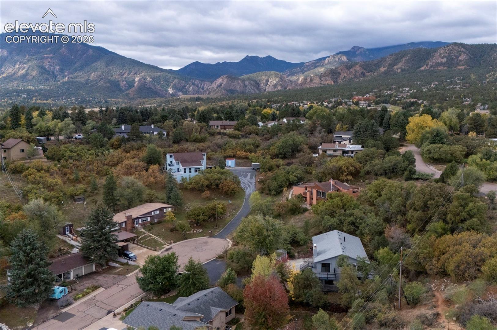 Aerial perspective featuring extensive mountain range backdrop, mature evergreen and deciduous vegetation, and established residential lots
