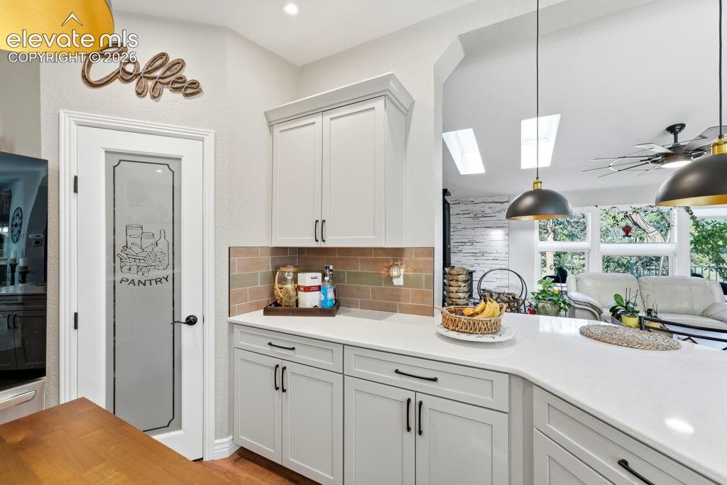 White shaker-style cabinetry with dark hardware, solid surface countertops, a tiled backsplash, and a pantry door with frosted glass