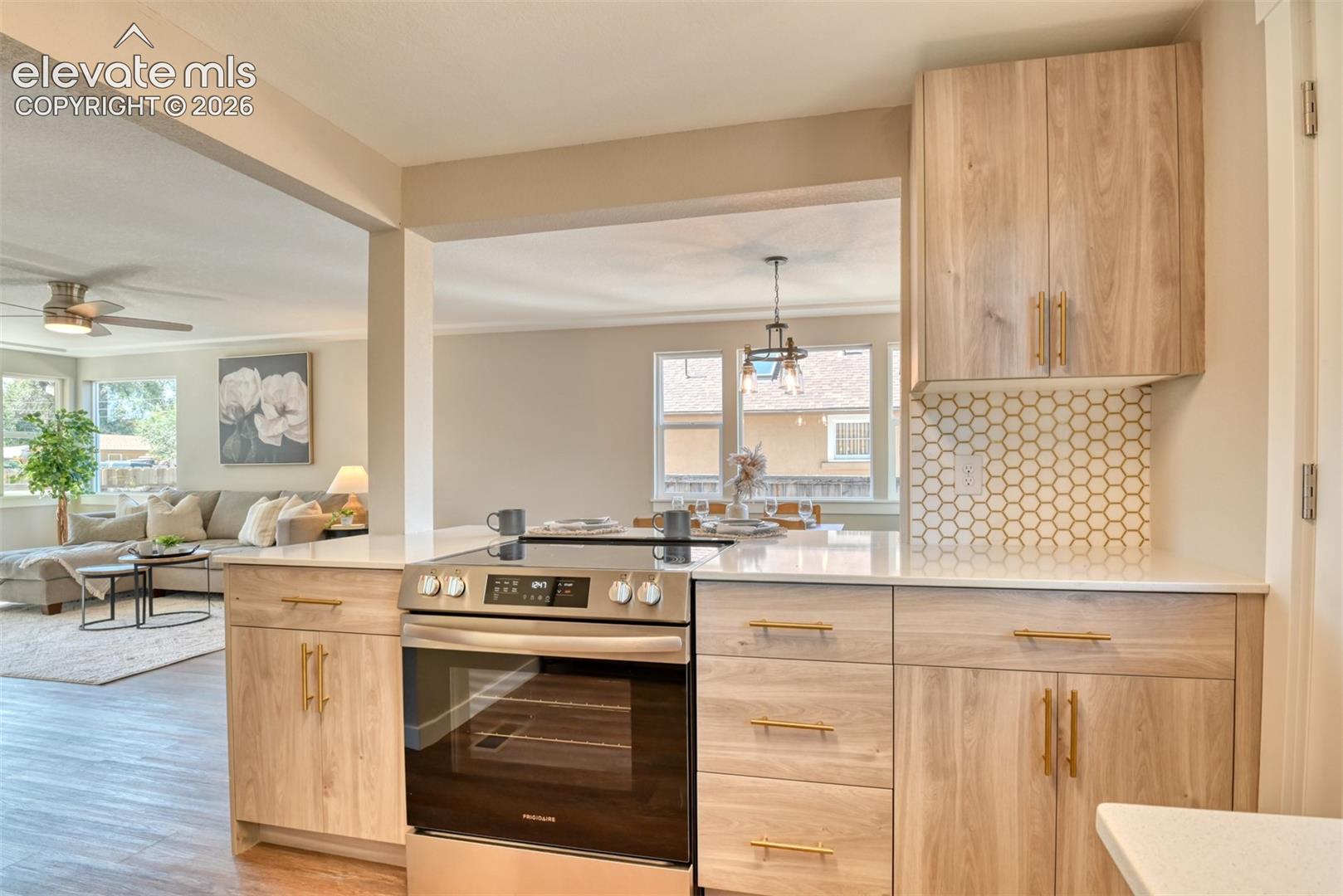 Wood-finish cabinetry with gold-tone hardware, white countertops, stainless steel range, and hexagonal tile backsplash