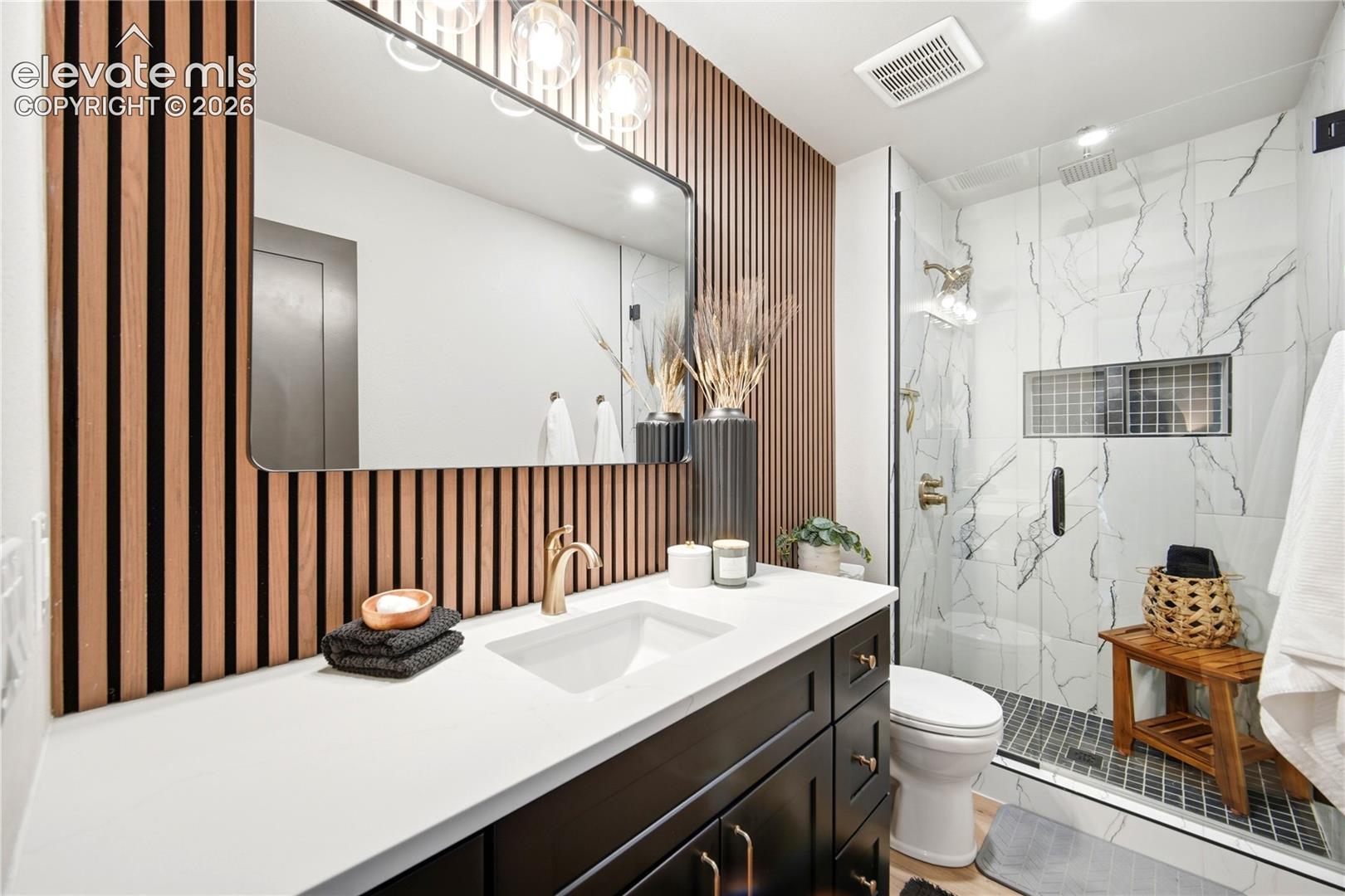 Bathroom vanity featuring a solid surface countertop, integrated sink, and brass-tone faucet hardware, set against a wood-slat accent wall