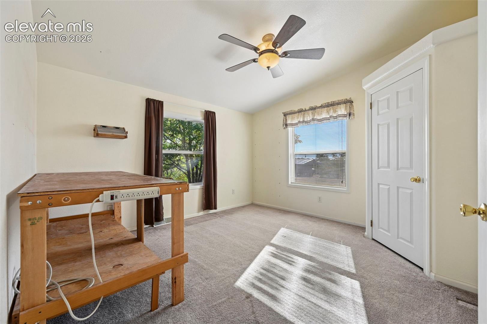 Neutral carpeted flooring, vaulted ceilings, multi-pane windows, and a central ceiling fan with an integrated light fixture