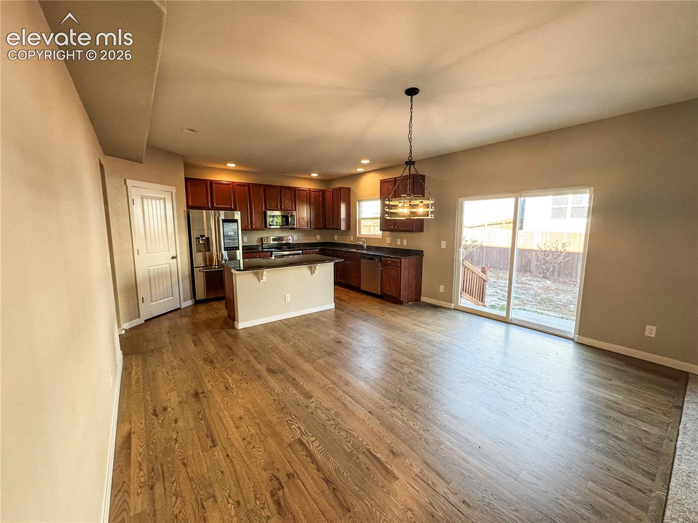 Kitchen featuring dark-toned cabinetry, stainless steel appliances, a peninsula with an integrated counter, wood-finish flooring, and a glass sliding door