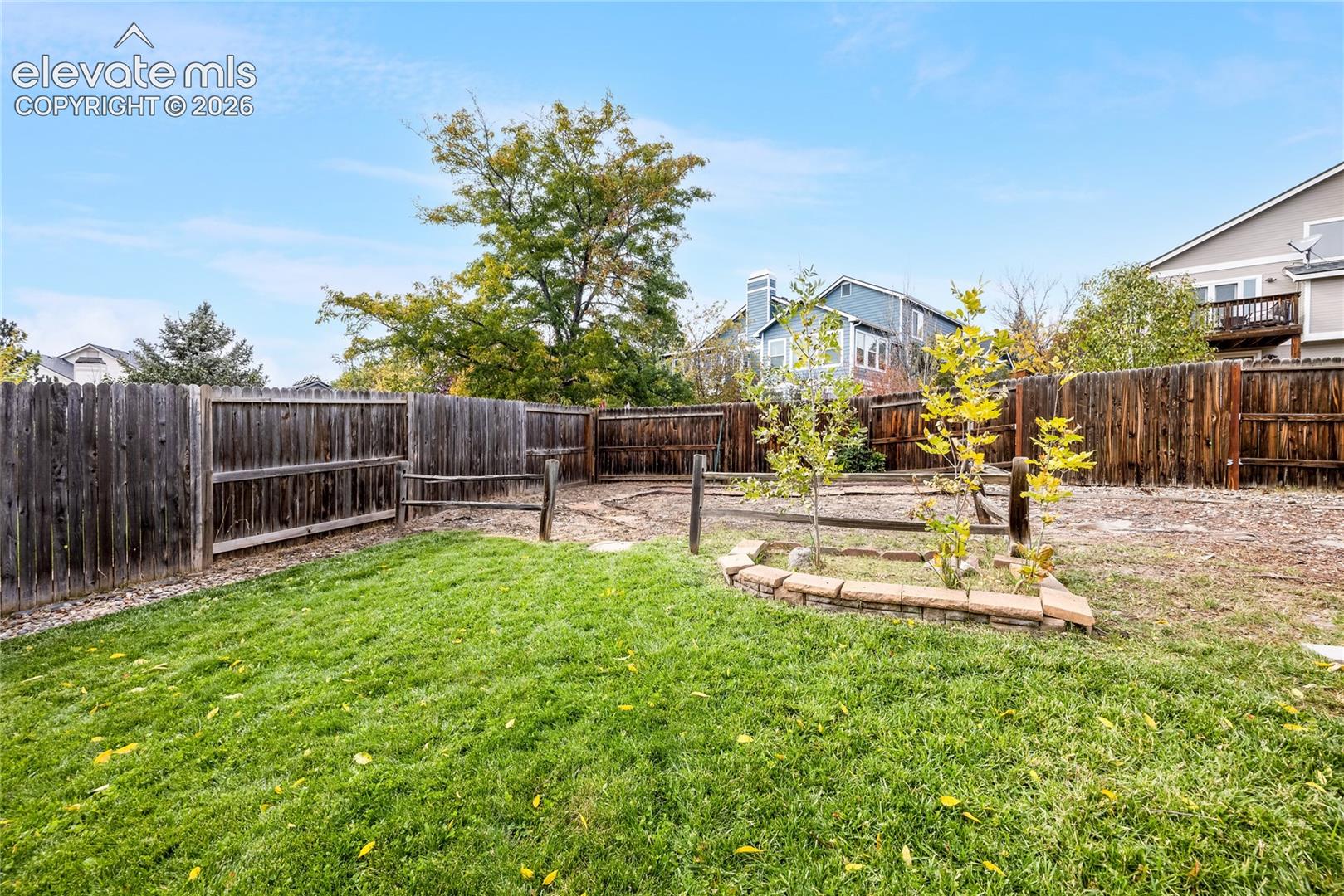 Fenced backyard featuring a manicured lawn, stone-border garden bed, and wood-post perimeter fencing