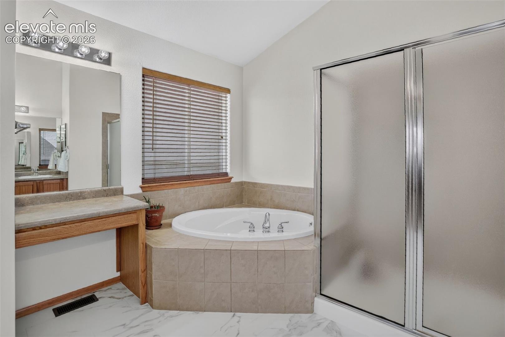 Bathroom featuring a built-in corner bathtub with tiled surround, a separate shower with frosted glass doors, and a vanity with a counter and mirror