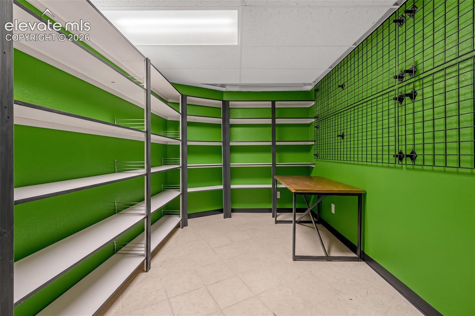 Integrated shelving units, grid wall storage, tile flooring, and a built-in desk with a wood-finish top