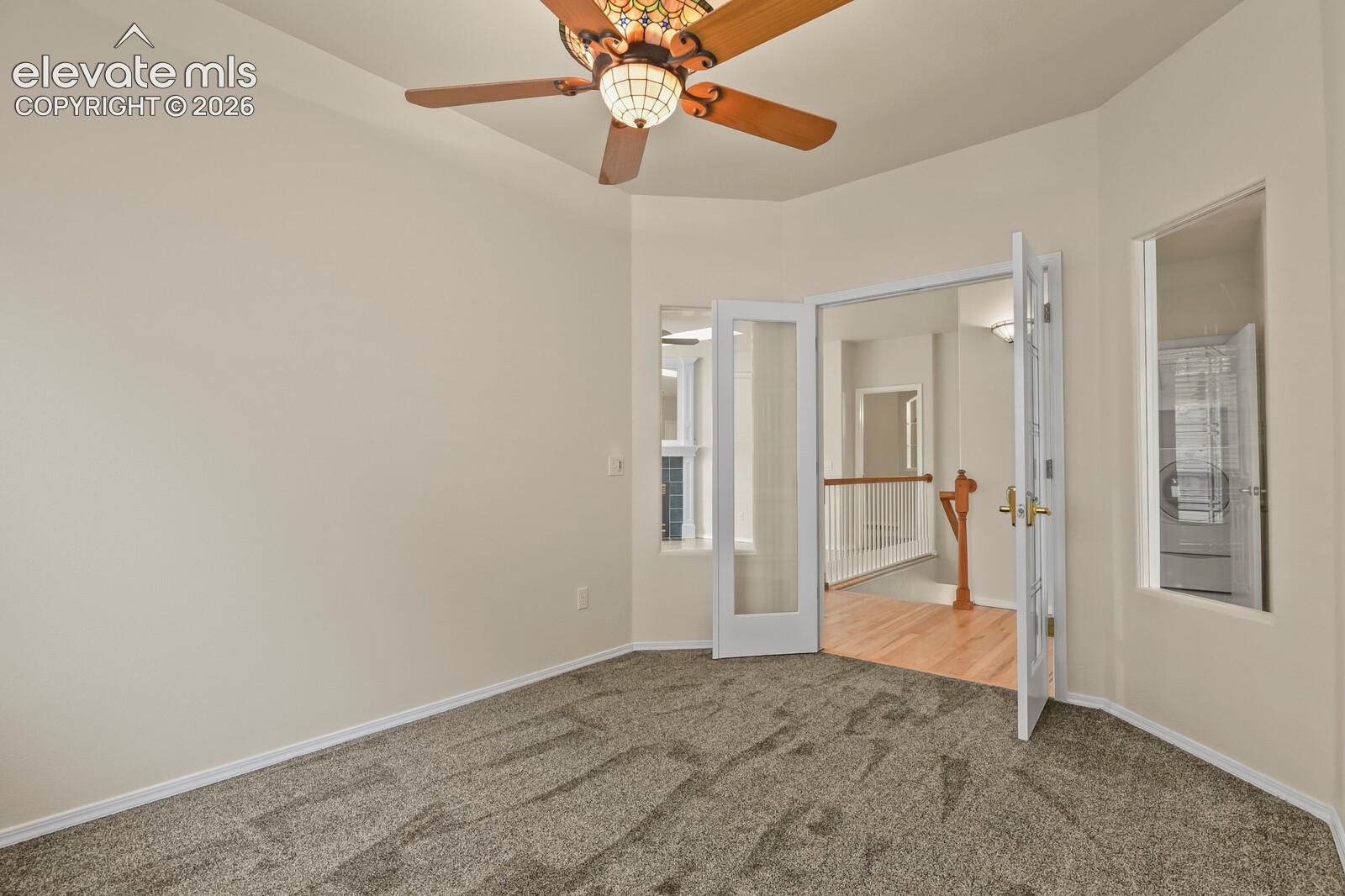 Interior room featuring neutral carpeting, a decorative stained-glass ceiling fan with wood-tone blades, white French doors, and glass-paneled walls