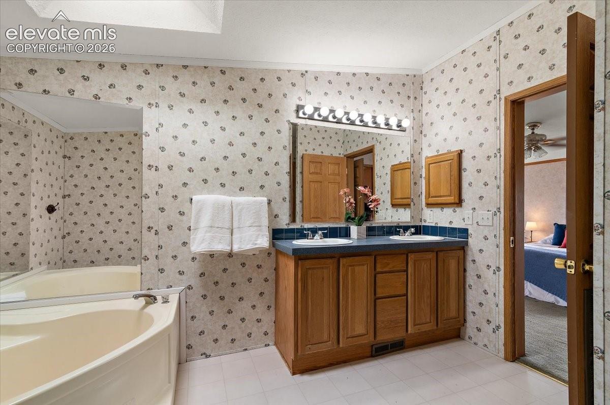 Dual vanity with integrated sinks and wood-finish cabinetry, above-mirror lighting, and a skylight