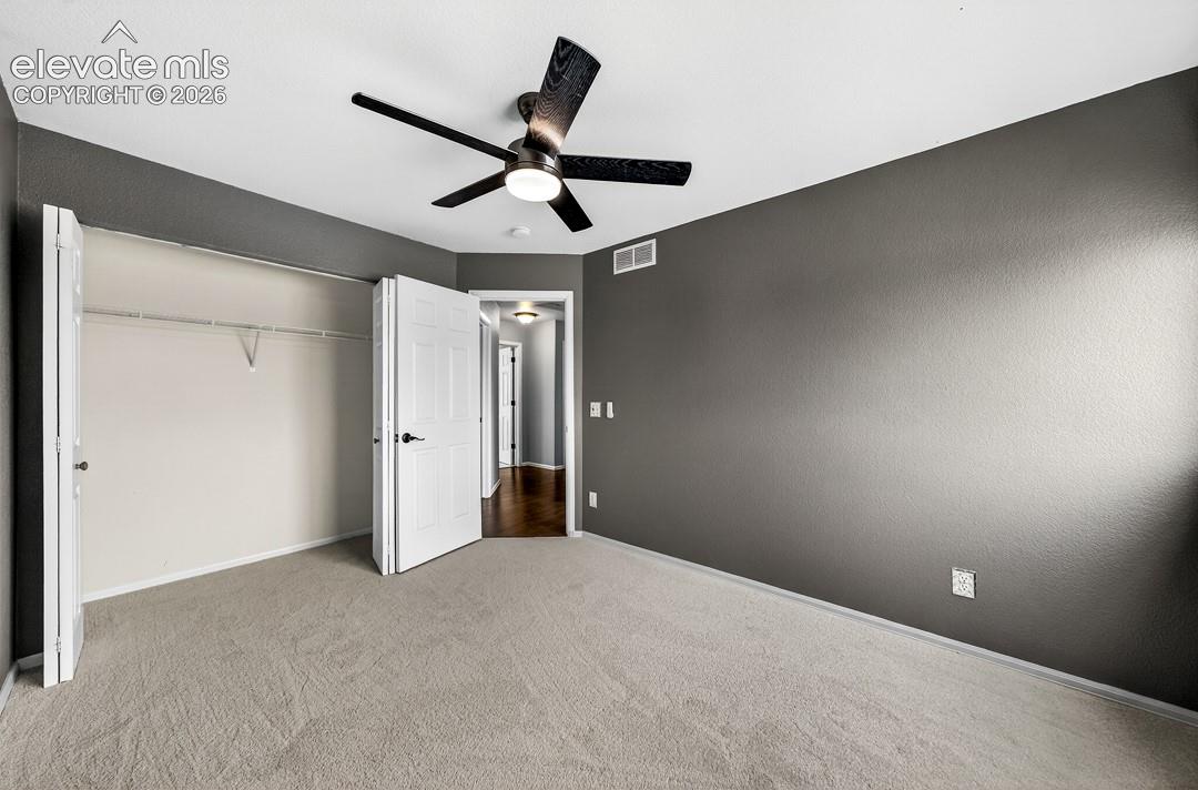 Room featuring neutral-toned carpeting, charcoal-painted walls, a ceiling fan with integrated lighting, and a bi-fold closet door