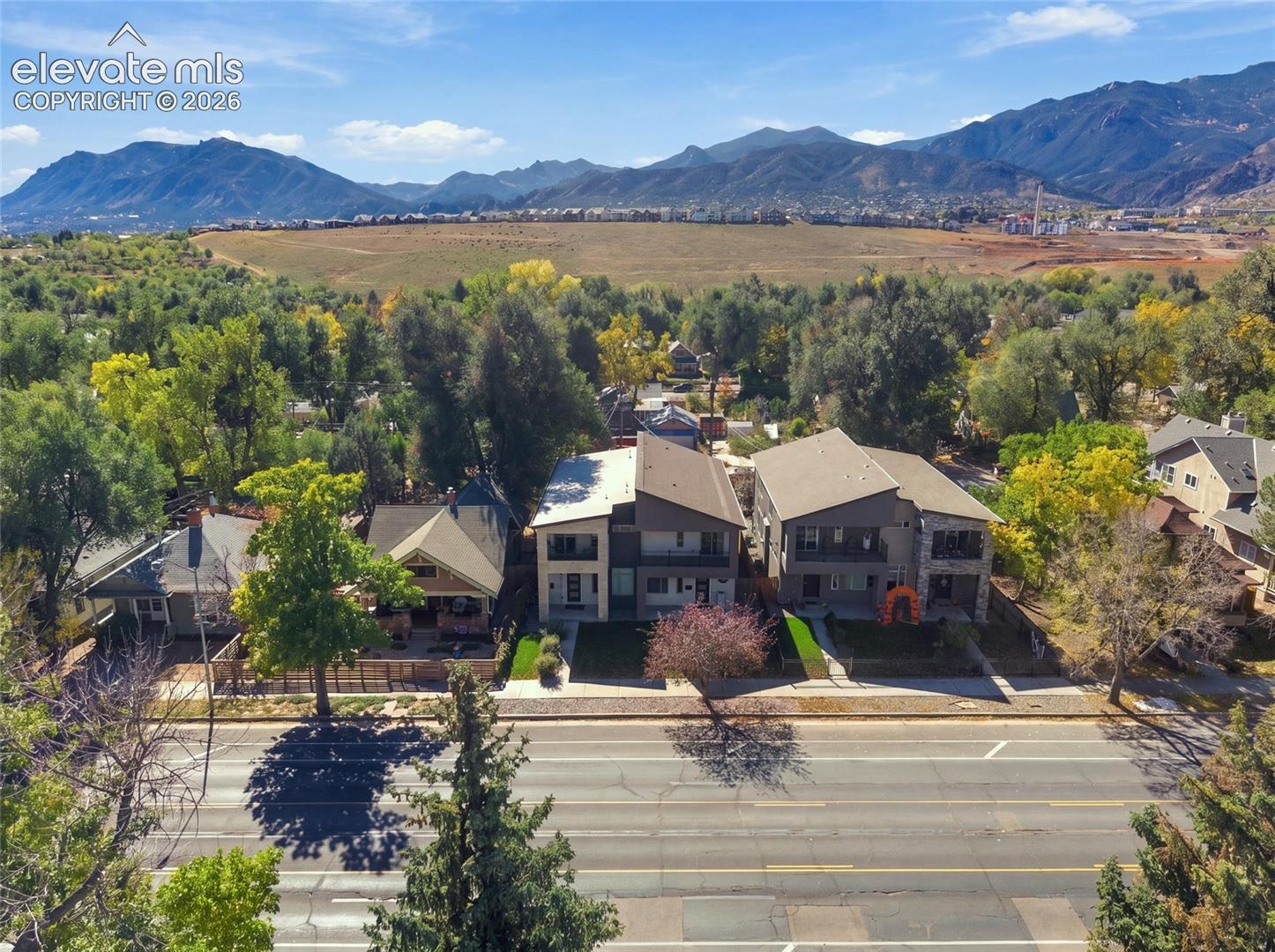 Aerial perspective featuring multi-level residential structures, mountainous backdrop, and mature tree-lined surroundings