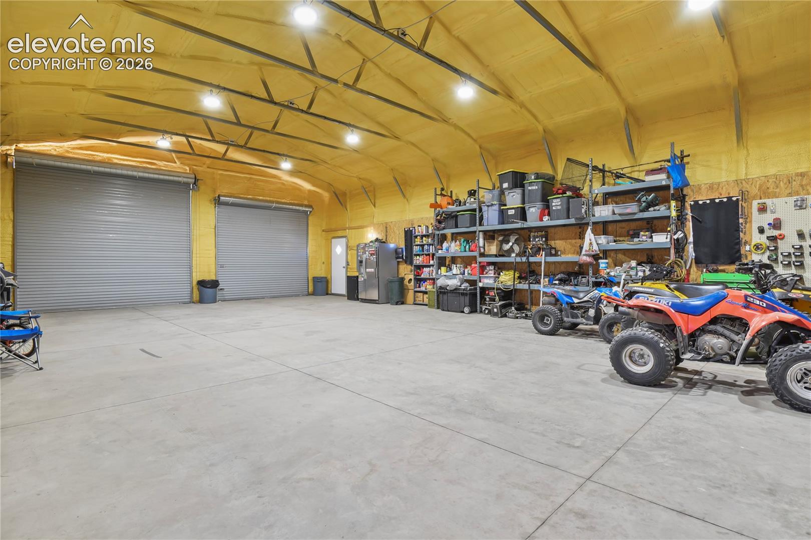 Spacious workshop featuring dual roll-up garage doors, concrete flooring, exposed insulated walls, and overhead recessed lighting