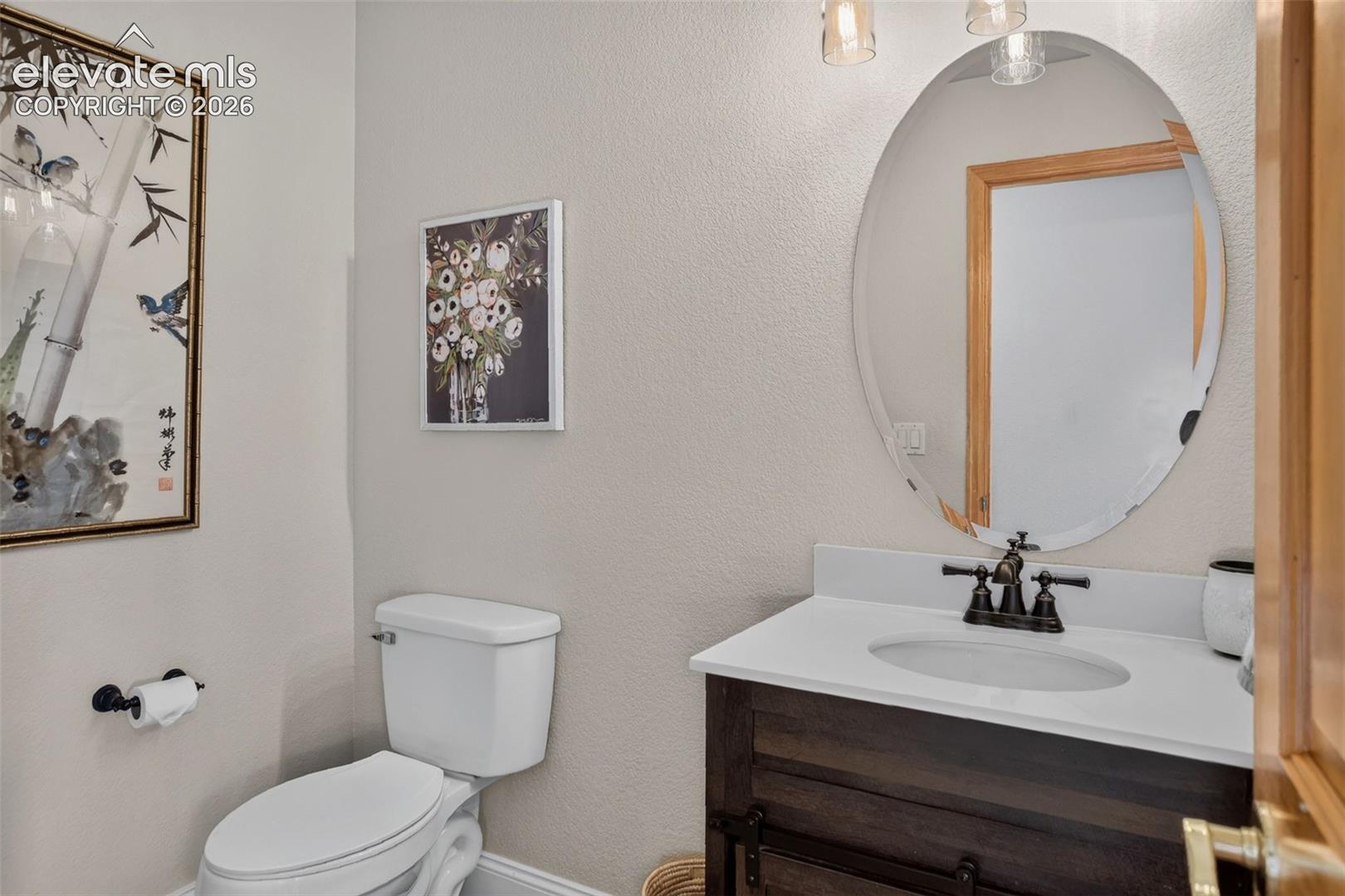 Compact powder room featuring a single-sink vanity with dark wood-finish cabinetry, a white countertop, and an oval mirror