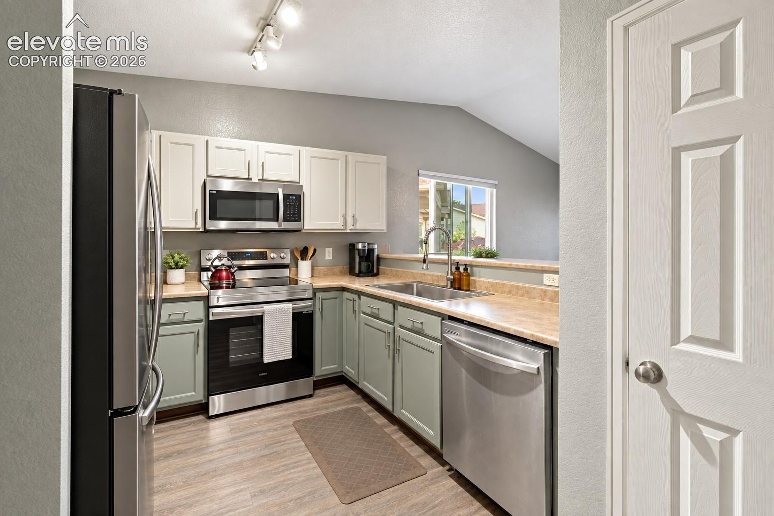 Kitchen featuring stainless steel appliances, wood-finish flooring, two-tone cabinetry, and a vaulted ceiling
