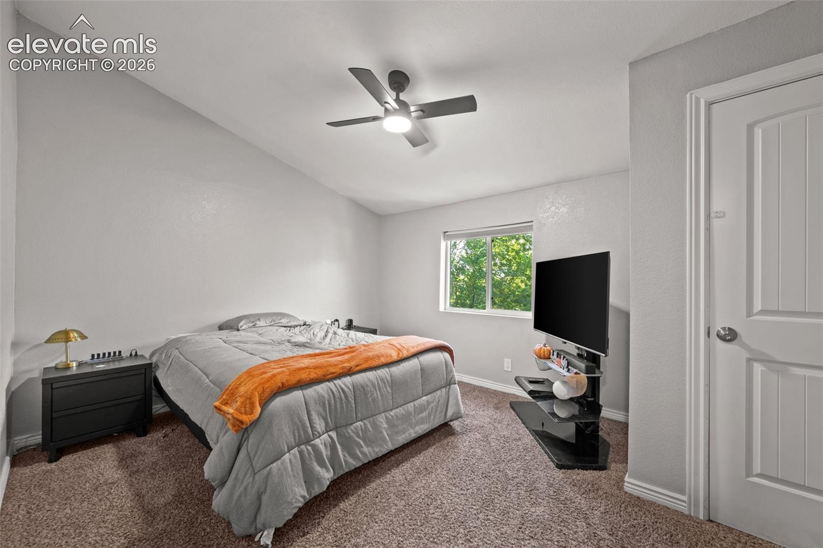 Vaulted ceiling, neutral wall tones, ceiling fan with integrated lighting, window with external greenery, and a paneled interior door