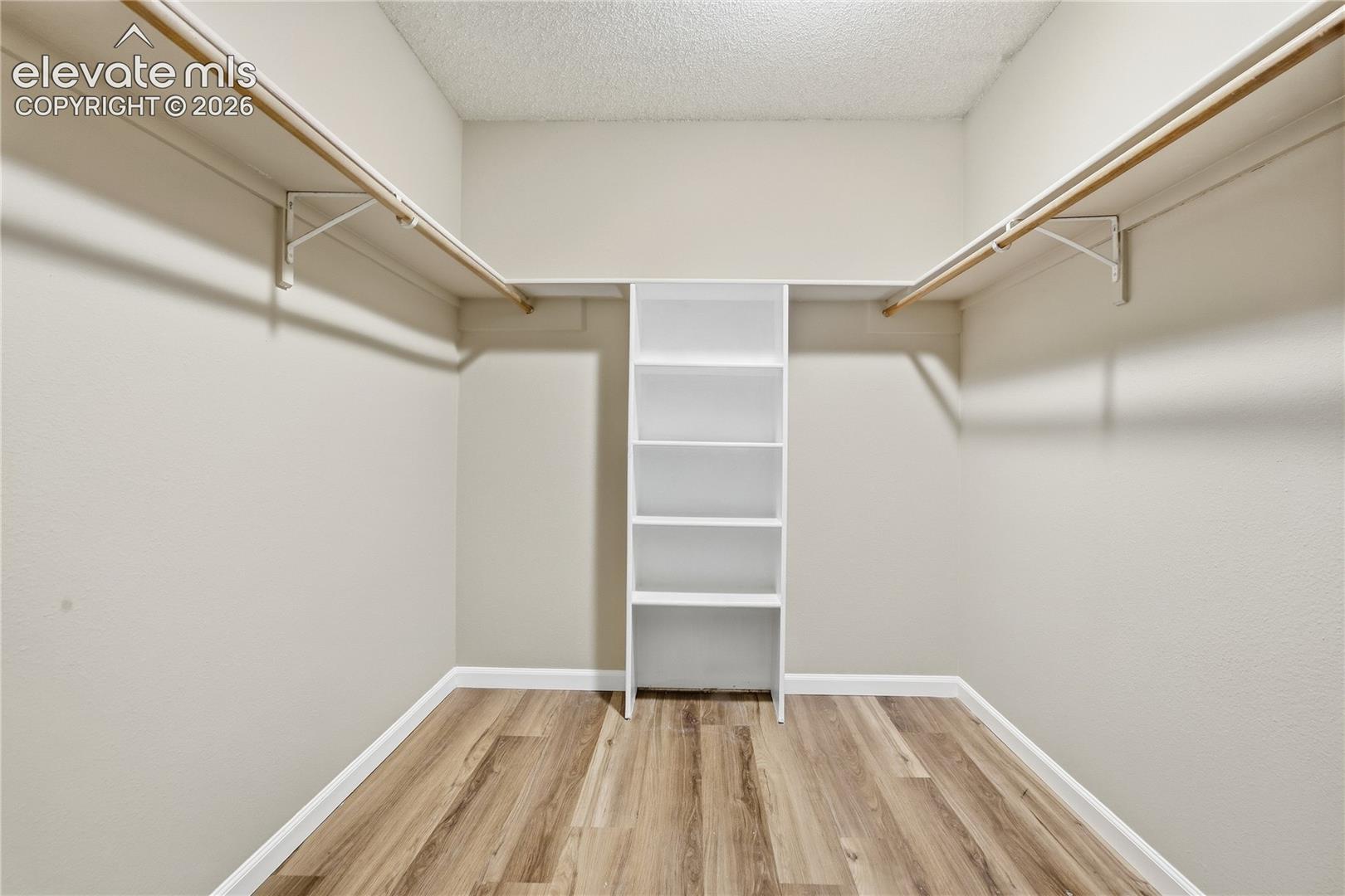 Walk-in closet featuring wood-finish flooring, built-in shelving, and dual hanging rods