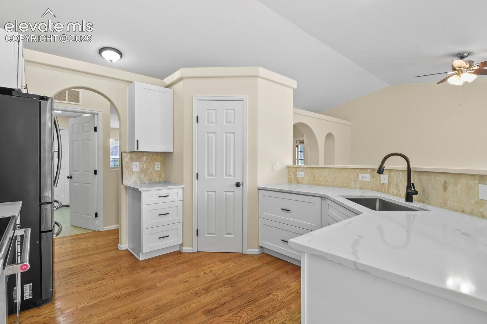 Updated kitchen featuring white shaker cabinetry, quartz countertops, a black gooseneck faucet, and wood-finish flooring